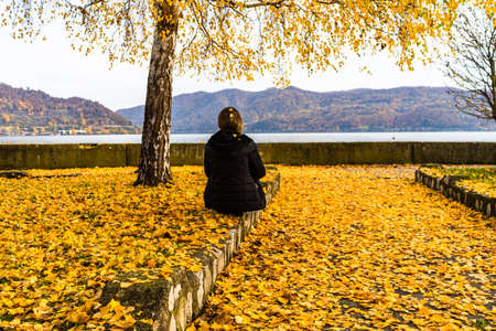 Autumn leaves fallen on standing alone woman on the autumn alley. Autumn landscape, orange foliage in a park in Orsova, Romaniaの写真素材
