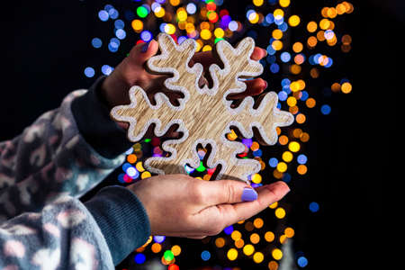 Holding Christmas snowflake decoration isolated on background with blurred lights. December season, Christmas composition.の写真素材