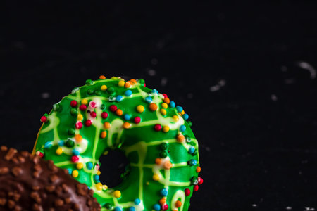 Fresh tasty colored donuts with sprinkles on black background