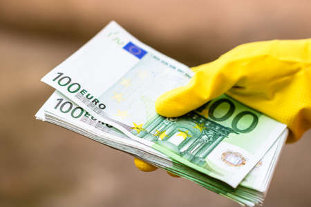 Hand with gloves receiving, giving or holding 100 EURO banknote, isolated on blurred backgroundの写真素材