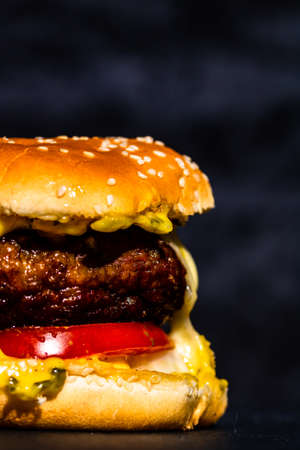 Detail of fresh tasty beef cheeseburger with melted cheese isolated on black backgroundの写真素材