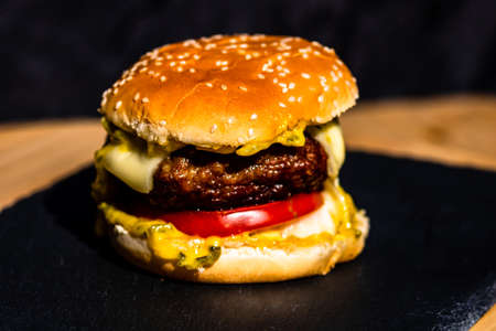 Detail of fresh tasty beef cheeseburger with melted cheese isolated on black backgroundの写真素材