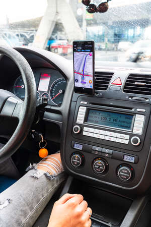 Using waze maps application on smartphone on car dashboard, Driver using maps app for showing the right route through the traffic of city on a rainy evening. Bucharest, Romania, 2020.のeditorial素材