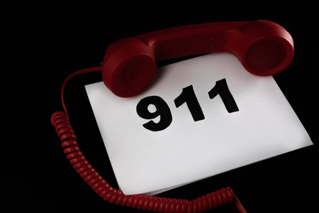 Call 911 and emergency call concept, text 911 on paper and phone isolated on black.