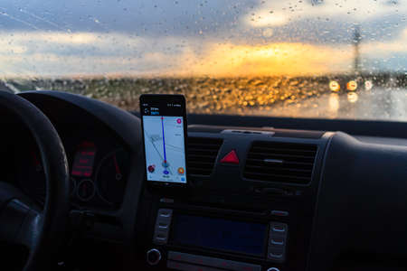 Using waze maps application on smartphone on car dashboard, Driver using maps app for showing the right route through the traffic of city at sunset on a rainy evening. Bucharest, Romania, 2020.のeditorial素材