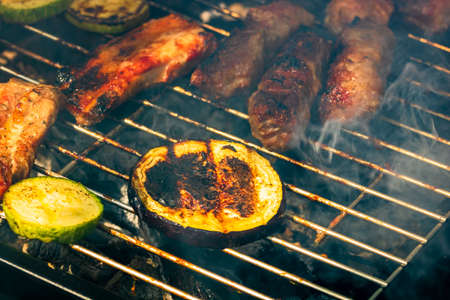 Grilling meat rolls called mici or mititei with vegetables on char barbecue. Charcoal grill with burning fireの写真素材