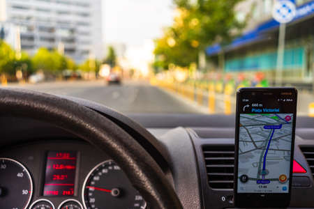In car dashboard view with smartphone showing Waze maps to show the way thru the city. Driver using Waze maps in Bucharest, Romania, 2020のeditorial素材