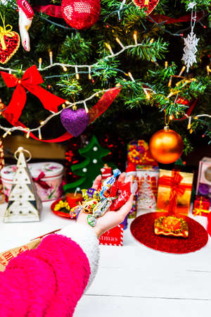 Hand holding chocolate candies in front of the Christmas tree. Decorating Christmass tree or unpacking the gifts. Bucharest, Romania, 2020のeditorial素材