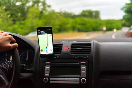 Driving and using waze maps application on smartphone on car dashboard, Driver using maps app for showing the right route through the traffic of city. Bucharest, Romania, 2020.のeditorial素材