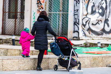 Single mom with child pushing baby stroller in Bucharest, Romania, 2022