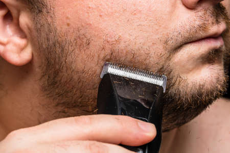 Man shaving or trimming his beard using a hair clipperの写真素材
