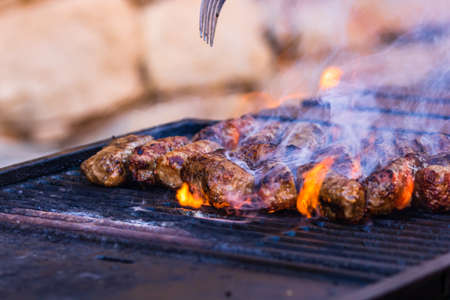 Preparing meat rolls called mici or mititei on barbecue. close up of grill with burning fire with flame and smoke.の写真素材