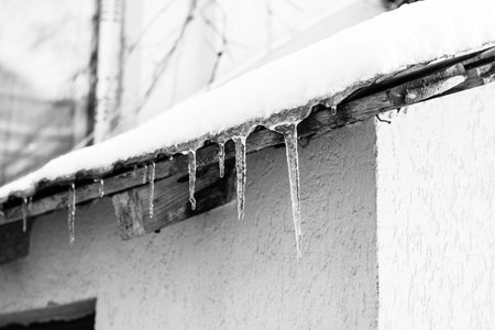 Roof covered with snow, icicles on roof isolated close up.
