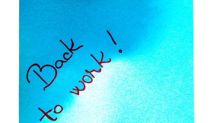 Back to work handwriting text close up isolated on blue paper with copy space. Writing text on memo post reminderの写真素材