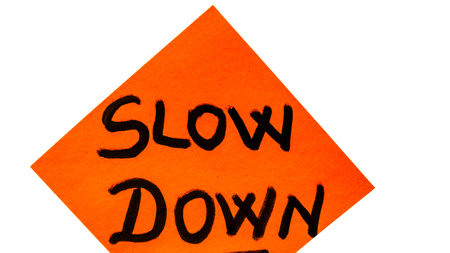 Slow down handwriting text close up isolated on yellow paper with copy space.の写真素材