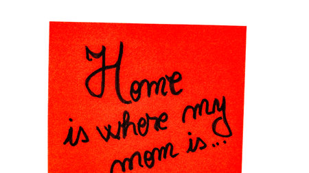Home is where my mom is handwriting text close up isolated on orange paper with copy space. Writing text on memo post reminderの写真素材