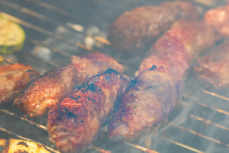 Grilling meat rolls called mici or mititei with vegetables on char barbecue. Charcoal grill with burning fireの写真素材
