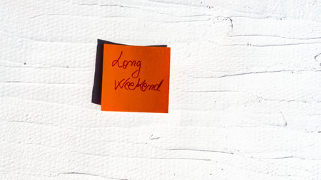 Handwriting text on memo post reminder. Long weekend on paper, on white and textured wall.  Copy...