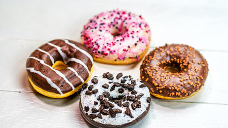 Colorful donuts on white wooden table. Sweet icing sugar food with glazed sprinkles, doughnut with frosting. Top view with copy spaceの写真素材