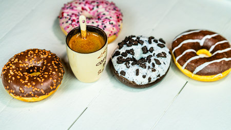 Colorful donuts and coffee cup on white wooden table. Sweet bakery with glazed sprinkles, breakfast concept. Top view with copy spaceの写真素材