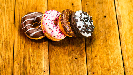 Colorful donuts on wooden table. Sweet icing sugar food with glazed sprinkles, doughnut with chocolate frosting. Top view with copy spaceの写真素材