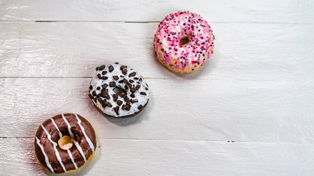 Colorful donuts on white wooden table. Sweet icing sugar food with glazed sprinkles, doughnut with frosting. Top view with copy spaceの写真素材