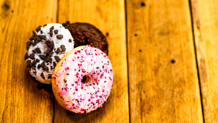 Colorful donuts on wooden table. Sweet icing sugar food with glazed sprinkles, doughnut with chocolate frosting. Top view with copy spaceの写真素材