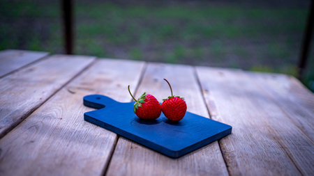 Close up of two strawberries on small black cutting board isolated outdoor on wooden table.の写真素材