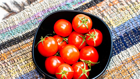 Detail of ripe cherry tomatoes in small black bowl on a rustic napkin. Ingredients and food conceptの写真素材