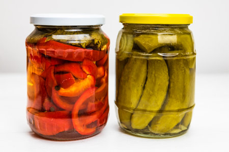 Glass jar with pickled red bell peppers and jar with pickled cucumbers (pickles) isolated.の写真素材