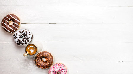 Colorful donuts on white wooden table. Sweet icing sugar food with glazed sprinkles, doughnut with frosting. Top view with copy spaceの写真素材