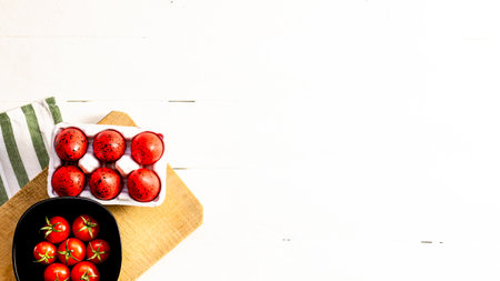 Top view of fresh ripe cherry tomatoes and red Easter eggs on a rustic white wooden table. Ingredients and food conceptの写真素材