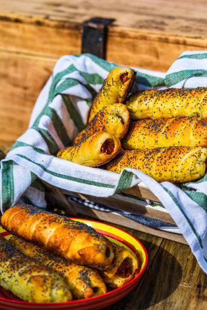 Sausages baked in dough sprinkled with salt and poppy seeds in a rustic composition. Sausages rolls, delicious homemade pastries.の写真素材