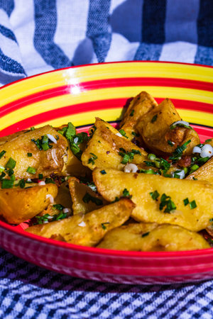 Close up with selective focus of fried potatoes with green onion, green garlic and spices in a colorful plate.の写真素材