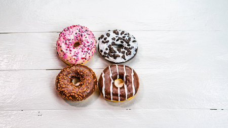 Colorful donuts on white wooden table. Sweet icing sugar food with glazed sprinkles, doughnut with frosting. Top view with copy spaceの写真素材