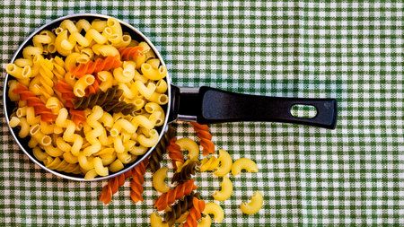 Small mini frying pan with tricolor raw fusilli pasta in a rustic composition.の写真素材