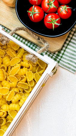 Top view of pasta in a wooden crate and fresh ripe cherry tomatoes in a black bowl on a rustic white wooden table. Ingredients and food conceptの写真素材