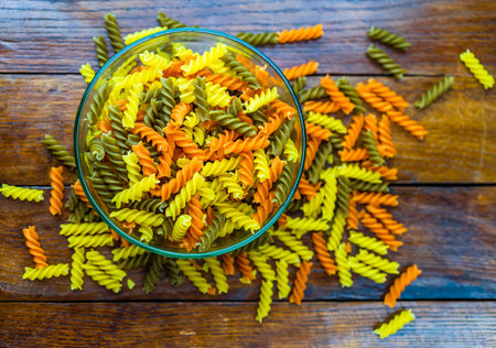 Composition of raw pasta uncooked tricolore fusilli, pasta twist shape. Close up and selective focus on colorful fusilli pasta. Fusilli pasta in bowl.の写真素材