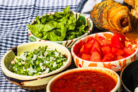 Rustic composition with sausages rolls and different bowls with sauce and chopped vegetables ( tomatoes, green lettuce, green onion, green garlic)の写真素材