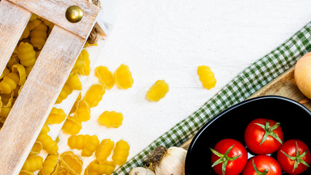 Top view of onions, garlic, pasta in a wooden crate and fresh ripe cherry tomatoes on a rustic white wooden table. Ingredients and food conceptの写真素材