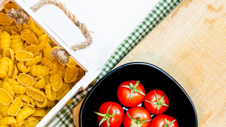 Top view of pasta in a wooden crate and fresh ripe cherry tomatoes in a black bowl on a rustic white wooden table. Ingredients and food conceptの写真素材
