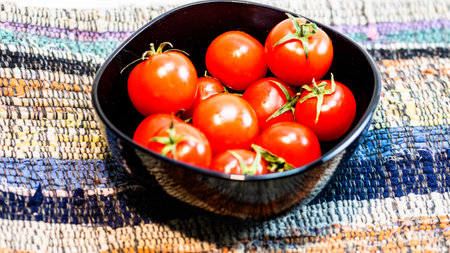 Detail of ripe cherry tomatoes in small black bowl on a rustic napkin. Ingredients and food conceptの写真素材