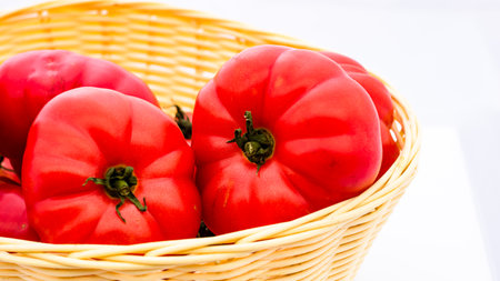 Fresh and tasty red tomatoes in wicker basket isolatedの写真素材