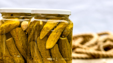 Glass jars with pickled red bell peppers and pickled cucumbers (pickles) isolated. Jars with variety of pickled vegetables. Preserved food concept in a rustic composition.の写真素材