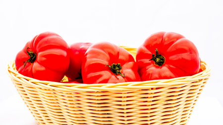 Fresh and tasty red tomatoes in wicker basket isolatedの写真素材