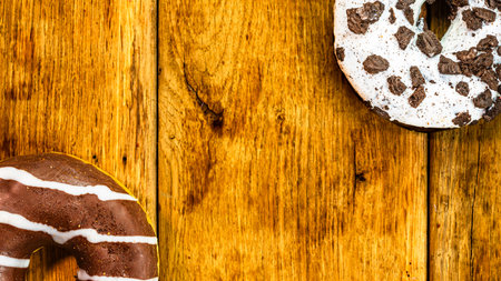 Colorful donuts on wooden table. Sweet icing sugar food with glazed sprinkles, doughnut with chocolate frosting. Top view with copy spaceの写真素材