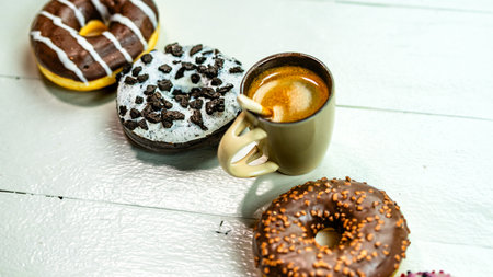 Colorful donuts and coffee cup on white wooden table. Sweet bakery with glazed sprinkles, breakfast concept. Top view with copy spaceの写真素材