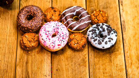 Colorful donuts on wooden table. Sweet icing sugar food with glazed sprinkles, doughnut with chocolate frosting. Top view with copy spaceの写真素材