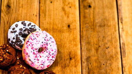 Colorful donuts on wooden table. Sweet icing sugar food with glazed sprinkles, doughnut with...