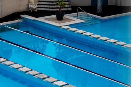 Clean swimming pool with clear blue water, bordered by white tiles and a striped deck, capturing the...